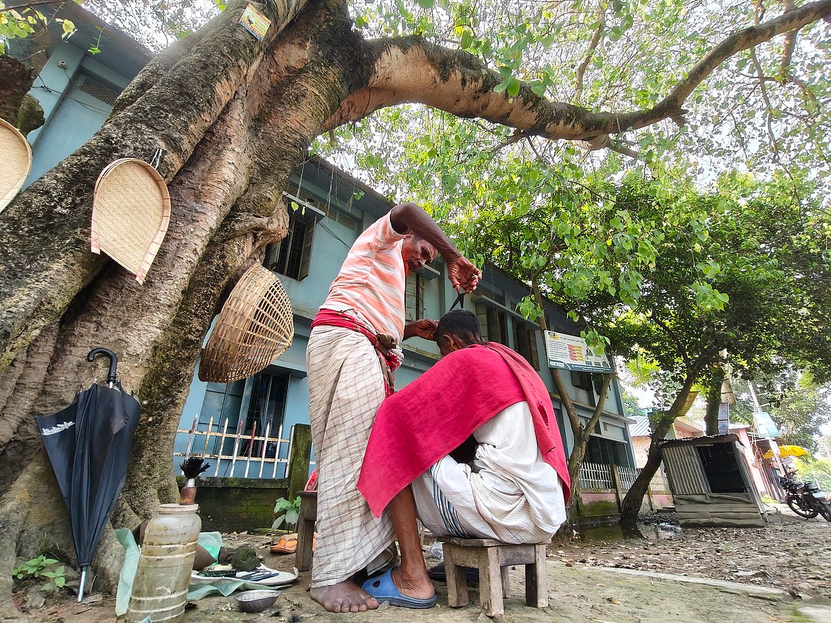 বটগাছের ছায়ায় বহু বছর ধরে চুল-দাড়ি কাটেন এই নরসুন্দর। দ্বীপচর, পাবনা, ২৮ সেপ্টেম্বর (ছবি: হাসান মাহমুদ)