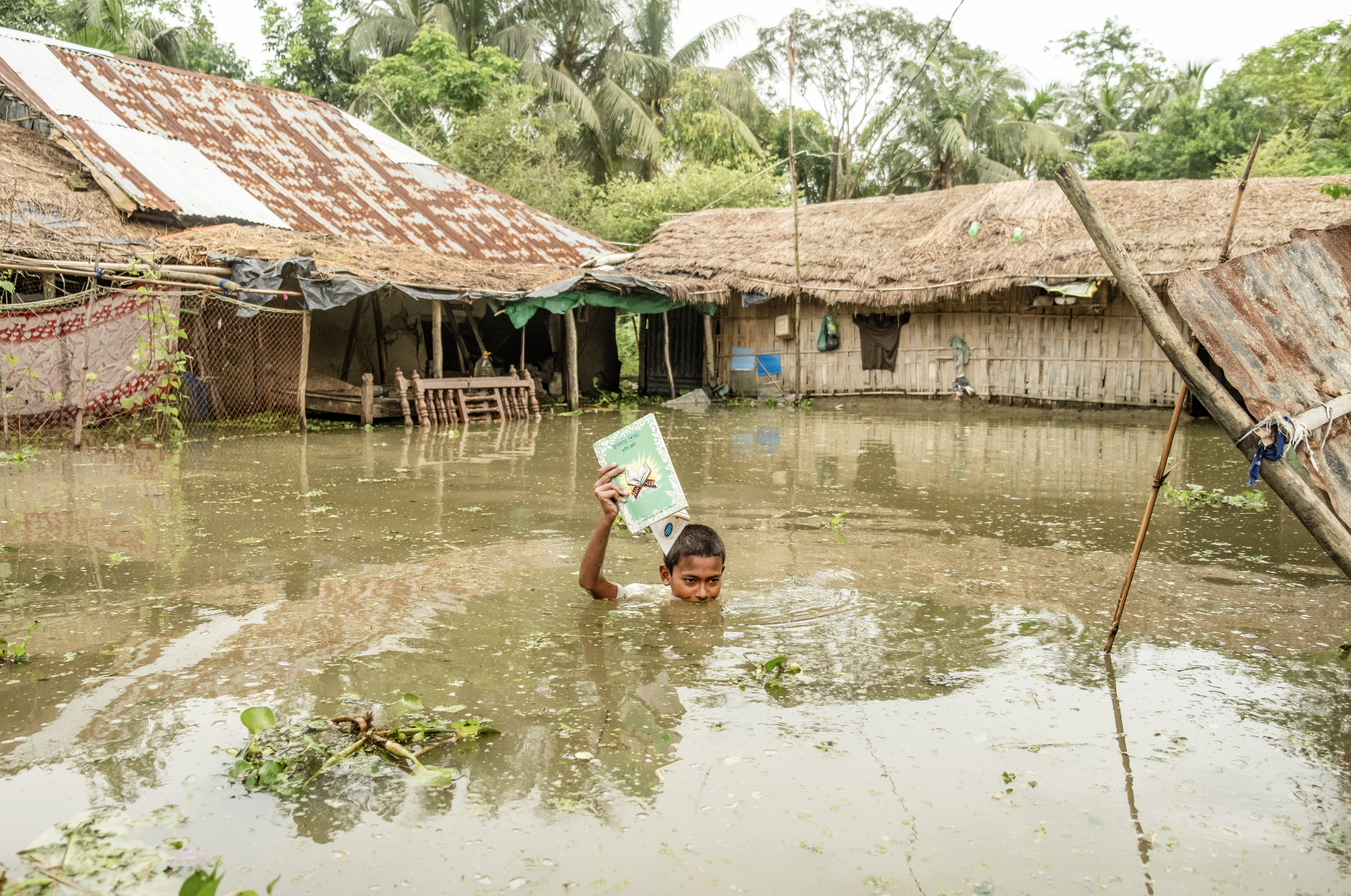 চট্টগ্রামের সাতকানিয়ায় ভারী বর্ষণে প্লাবিত গ্রামে বই মাথার ওপর তুলে পানি পার হচ্ছে এক স্কুলছাত্র; ২০২৬ সালের ১০ জুলাই তোলা ছবি। ছবি: Md shameem ul islam / উইকিমিডিয়া কমন্স (CC BY 4.0)